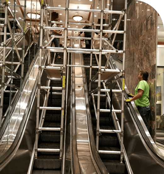 Escalators under construction with metal scaffolding and a worker in a green shirt.
